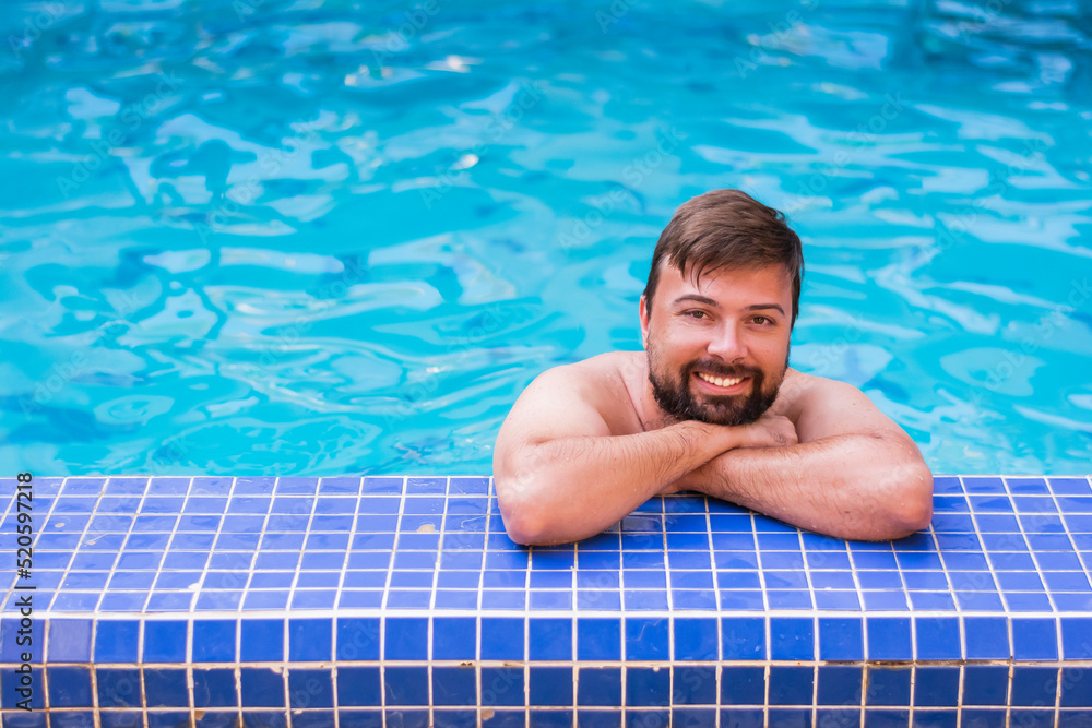 Portrait of a man 30 years old smiling positive naked in a blue pool resting on a weekend or vacation in the summer on a sunny day. Concept: rest in hotels by the pool 