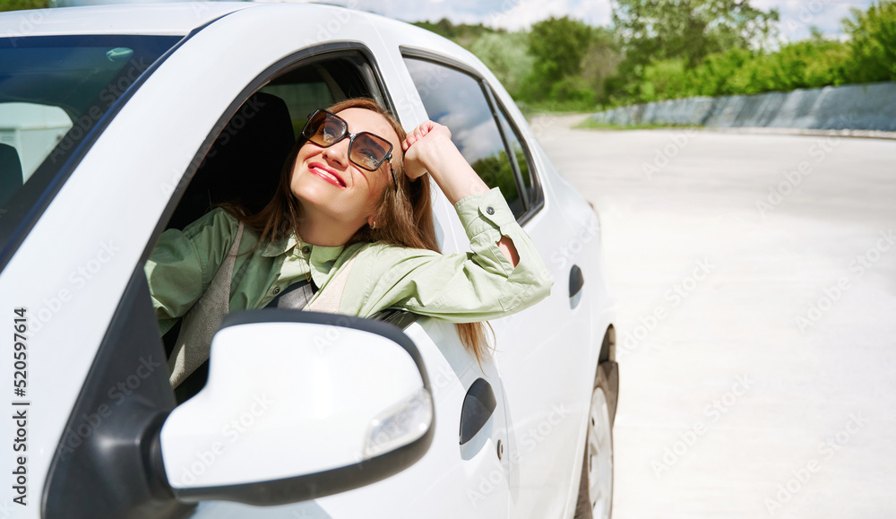 Happy young woman wearing sun glasses enjoys buying a new car or a rental car. The concept of buying a new car, renting and freedom of movement