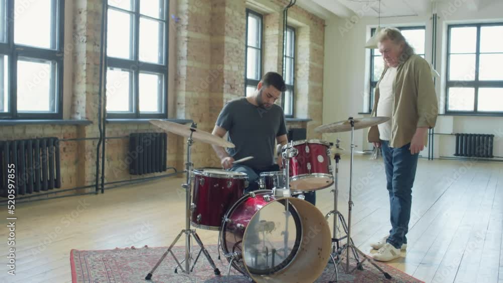Zoom in shot of senior musician teaching young man how to play drums in studio Zoom in shot of senior musician teaching young man how to play drums in studio