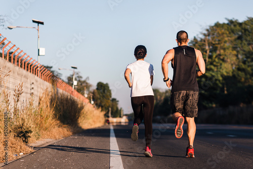 Runner wearing face mask while running together on the road from back view. Sportive man and woman jogging on street in the afternoon during coronavirus outbreak.