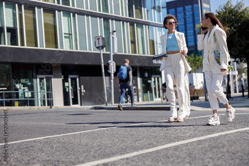 Two happy woman in trendy outfits laugh and walk outside on background of modern building