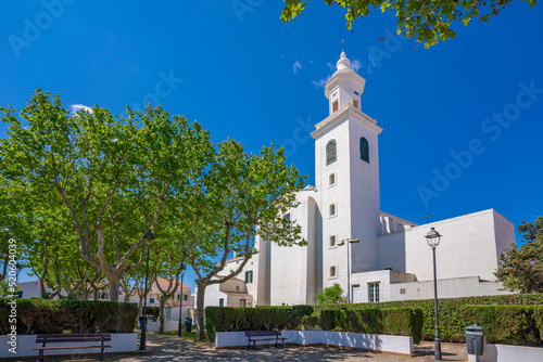 View of whitewashed Catholic Church framed by trees against blue sky, Sant Lluis, Menorca, Balearic Islands, Spain photo