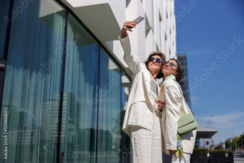 Wallpaper Mural Two smiling woman in trendy outfits making selfie on background of modern building Torontodigital.ca