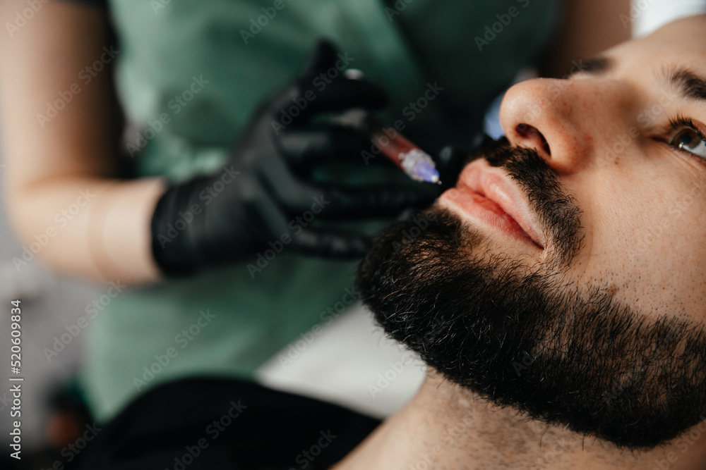 Fototapeta premium Beauty treatments for a stylish young man with a beard. Beautician makes beauty injections in a man's face