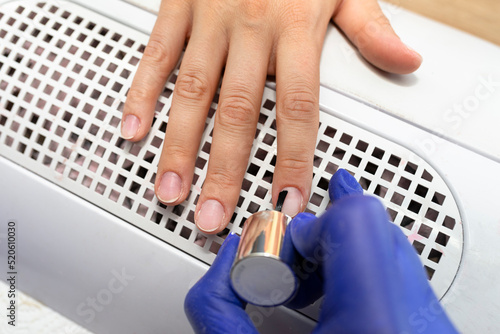 Applying the primer to ground fingernails  the manicurist wears blue latex gloves.