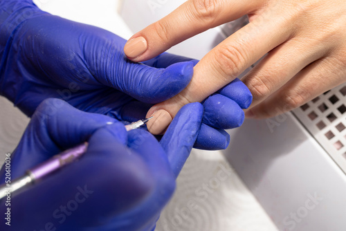 The manicurist paints the nails beige with hybrid varnish  a thin brush in blue latex gloves.