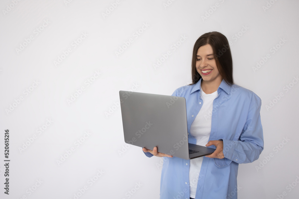 Smiling woman with white teeth in a blue shirt and a white t-shirt holds a laptop on a white background isolate. Concept: female freelancer. Woman in casual clothes. Mockup place for text. banner Smiling woman with white teeth in a blue shirt and a white t-shirt holds a laptop on a white background isolate. Concept: female freelancer. Woman in casual clothes. Mockup place for text. banner