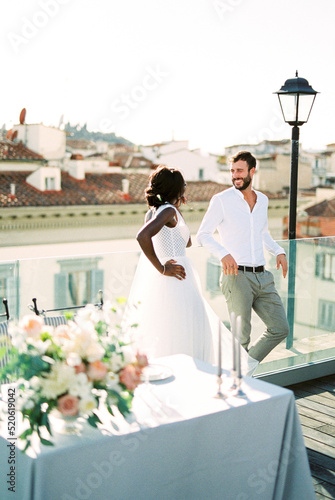 Bride stands next to groom near the table on the roof of the building