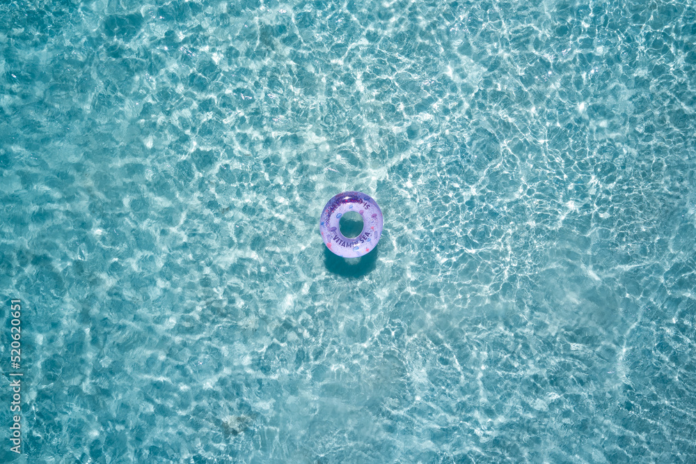 Pool ring in purple color on transparent water top view. Ring for the pool on the water air view. Ring for the pool with the inscription vitamin sea.