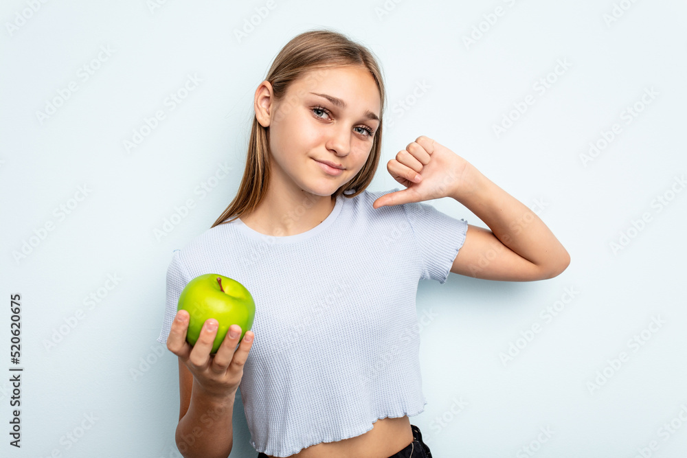 Young caucasian girl holding an apple isolated on blue background feels proud and self confident, example to follow. Young caucasian girl holding an apple isolated on blue background feels proud and self confident, example to follow.