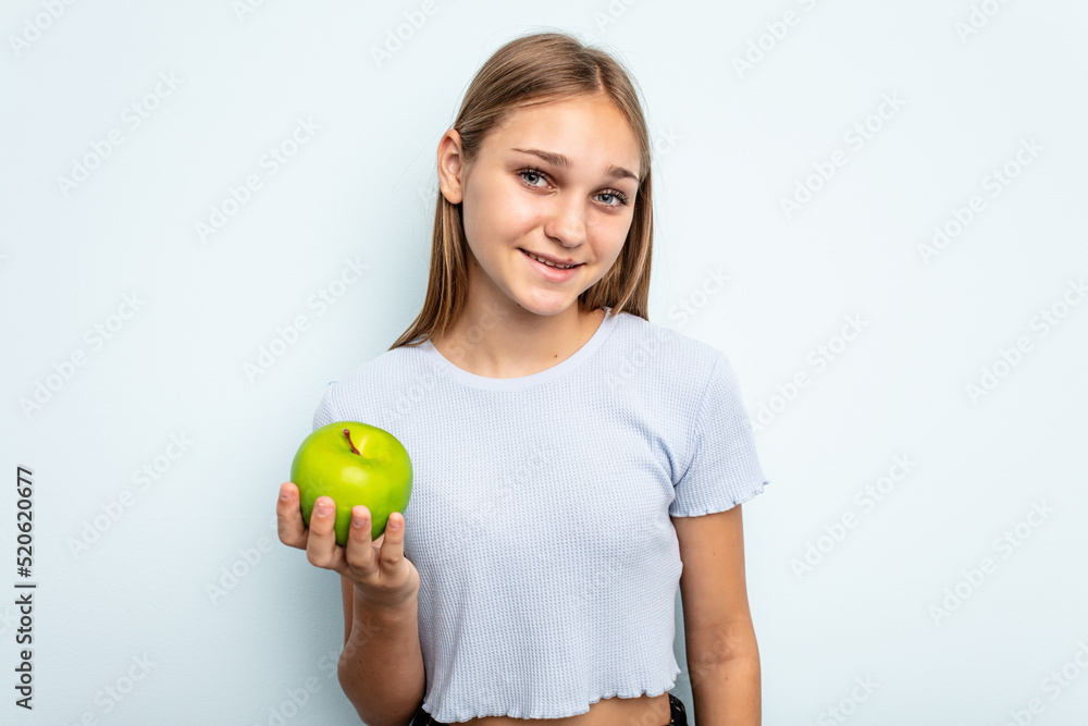 Young caucasian girl holding an apple isolated on blue background happy, smiling and cheerful. Young caucasian girl holding an apple isolated on blue background happy, smiling and cheerful.