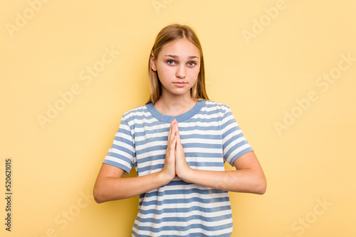 Young caucasian girl isolated on yellow background praying, showing devotion, religious person looking for divine inspiration.