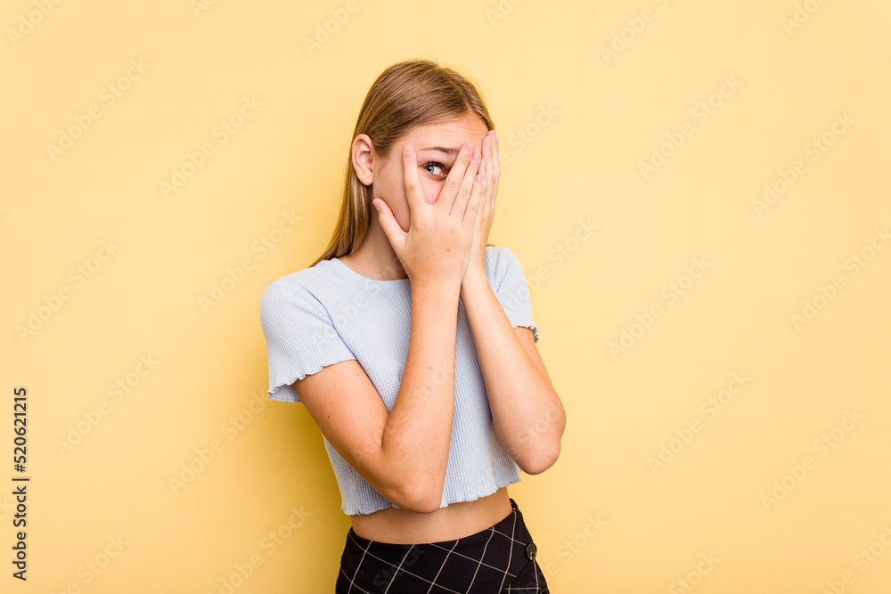 Young caucasian girl isolated on yellow background blink through fingers frightened and nervous. Young caucasian girl isolated on yellow background blink through fingers frightened and nervous.