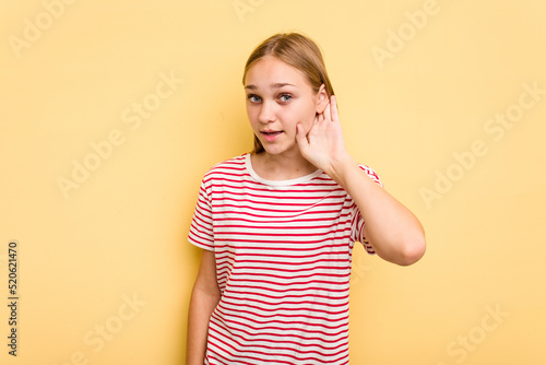 Young caucasian girl isolated on yellow background trying to listening a gossip.