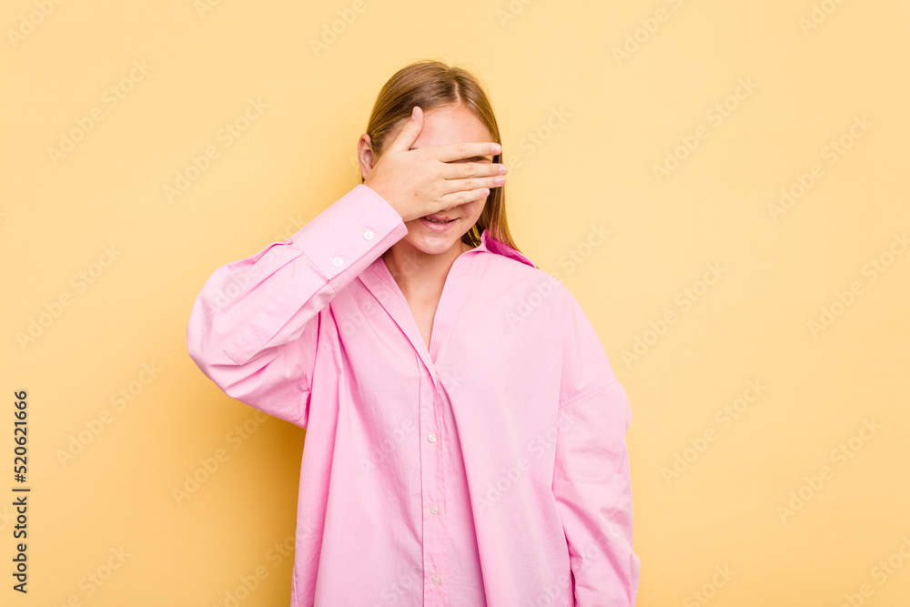 Young caucasian girl isolated on yellow background covers eyes with hands, smiles broadly waiting for a surprise. Young caucasian girl isolated on yellow background covers eyes with hands, smiles broadly waiting for a surprise.