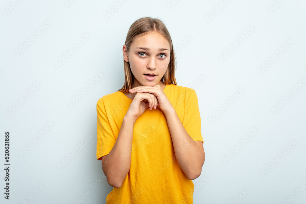 Young caucasian girl isolated on blue background praying for luck, amazed and opening mouth looking to front. Young caucasian girl isolated on blue background praying for luck, amazed and opening mouth looking to front.