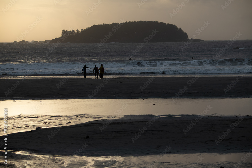 Surfers strolling beach at sunset in Tofino BC