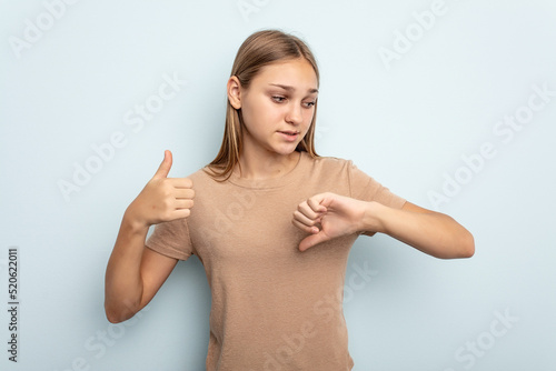 Young caucasian girl isolated on blue background showing thumbs up and thumbs down, difficult choose concept