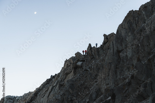 Climbers exposed on ridge line in front of moon against the sky photo