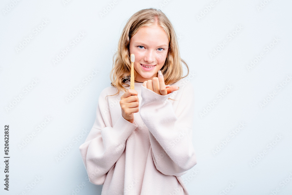 Caucasian teen girl holding a toothbrush isolated on blue background pointing with finger at you as if inviting come closer. Caucasian teen girl holding a toothbrush isolated on blue background pointing with finger at you as if inviting come closer.