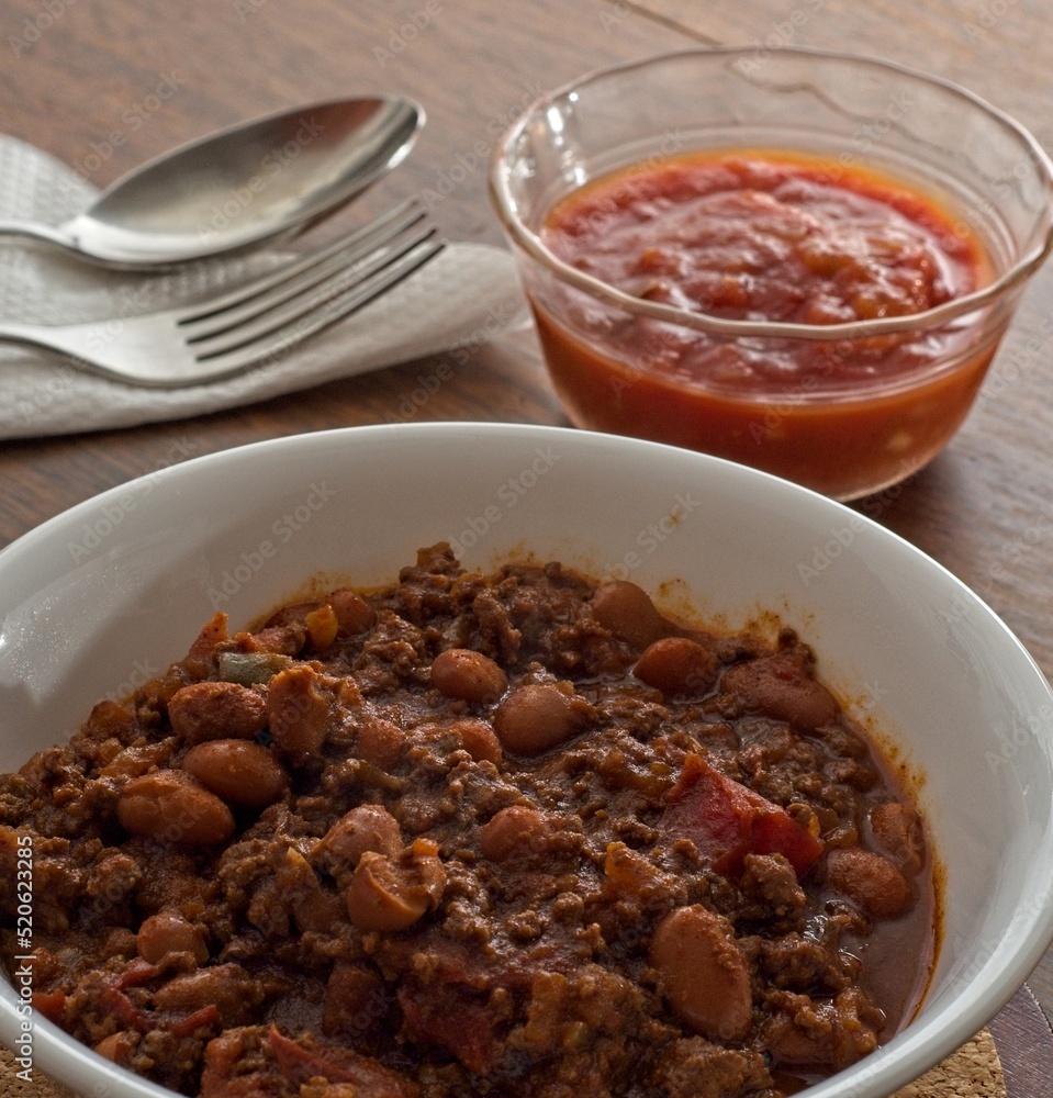 Close-up bowl of chili con carne with salsa bowl flatware napkin in background Close-up bowl of chili con carne with salsa bowl flatware napkin in background