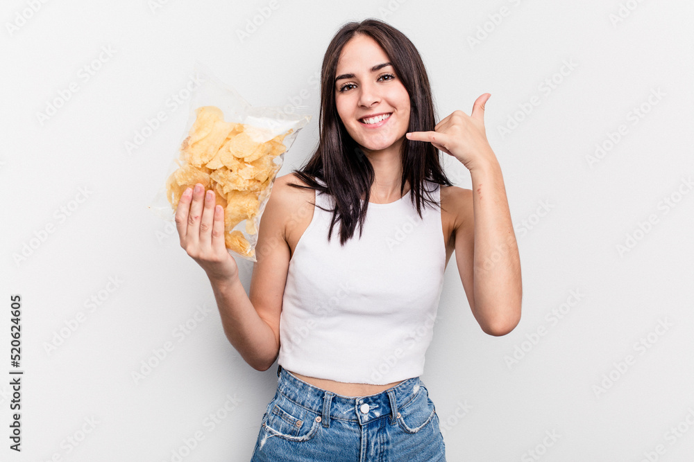 Young caucasian woman holding a bag of chips isolated on white background showing a mobile phone call gesture with fingers. Young caucasian woman holding a bag of chips isolated on white background showing a mobile phone call gesture with fingers.