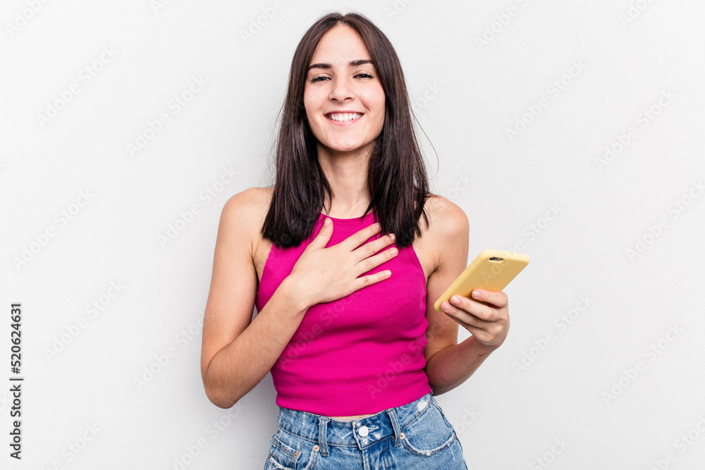 Young caucasian woman holding mobile phone isolated on white background laughs out loudly keeping hand on chest. Young caucasian woman holding mobile phone isolated on white background laughs out loudly keeping hand on chest.