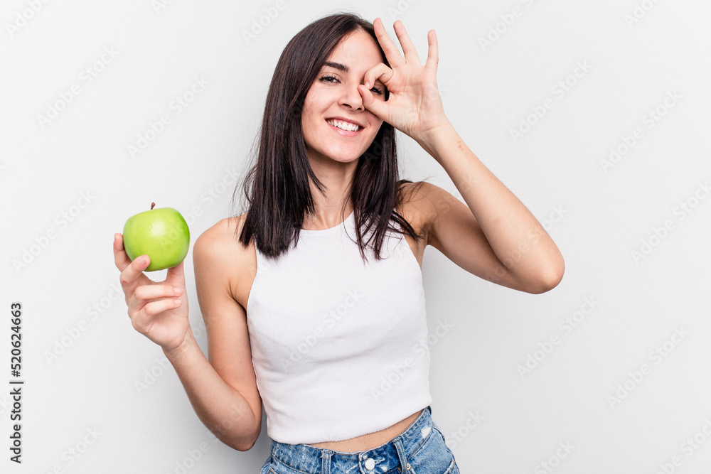 Young caucasian woman holding an apple isolated on white background excited keeping ok gesture on eye. Young caucasian woman holding an apple isolated on white background excited keeping ok gesture on eye.