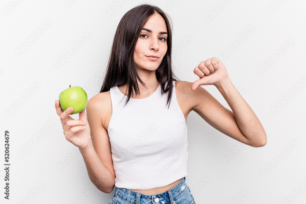 Young caucasian woman holding an apple isolated on white background showing a dislike gesture, thumbs down. Disagreement concept. Young caucasian woman holding an apple isolated on white background showing a dislike gesture, thumbs down. Disagreement concept.