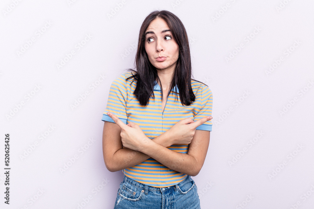 Young caucasian woman isolated on pink background points sideways, is trying to choose between two options.