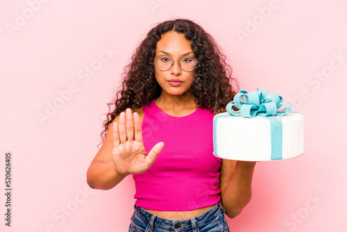 Young caucasian woman holding a cake isolated on pink background standing with outstretched hand showing stop sign, preventing you.