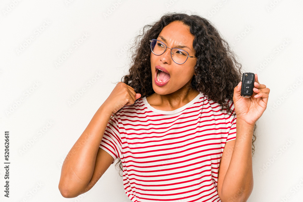 Young hispanic woman holding car keys isolated on white background raising fist after a victory, winner concept. Young hispanic woman holding car keys isolated on white background raising fist after a victory, winner concept.