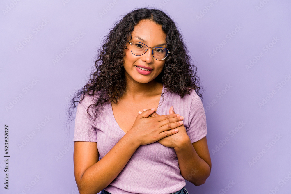 Young hispanic woman isolated on purple background has friendly expression, pressing palm to chest. Love concept. Young hispanic woman isolated on purple background has friendly expression, pressing palm to chest. Love concept.