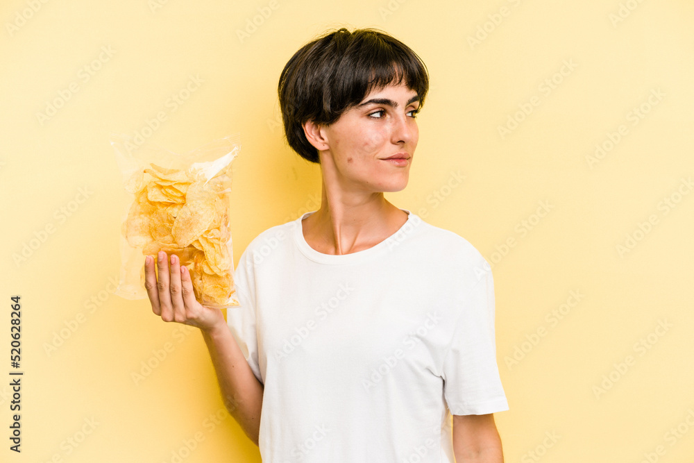 Young caucasian man holding crisps isolated on yellow background looks aside smiling, cheerful and pleasant. Young caucasian man holding crisps isolated on yellow background looks aside smiling, cheerful and pleasant.