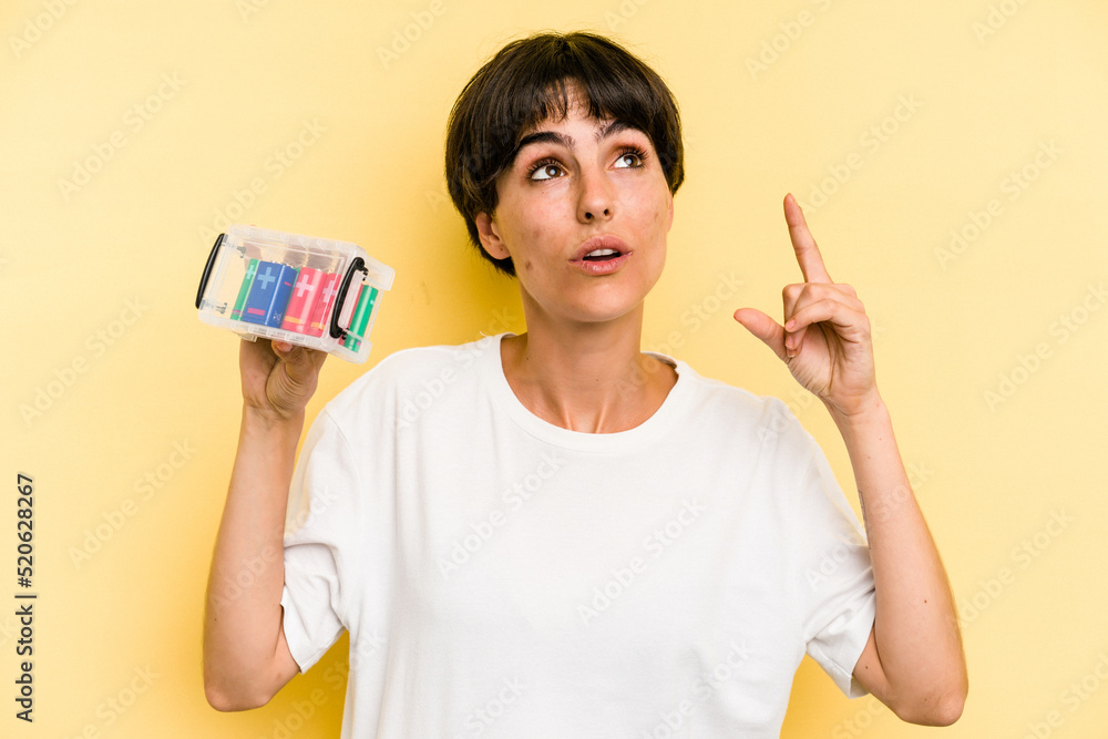 Young caucasian woman holding a batteries box isolated on yellow background pointing upside with opened mouth.