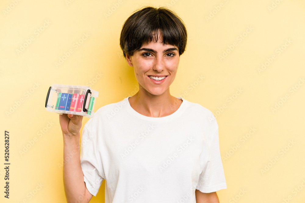 Young caucasian woman holding a batteries box isolated on yellow background happy, smiling and cheerful. Young caucasian woman holding a batteries box isolated on yellow background happy, smiling and cheerful.