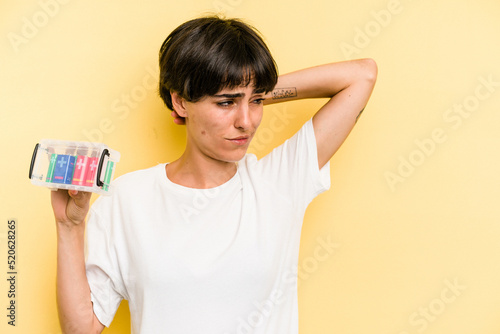 Young caucasian woman holding a batteries box isolated on yellow background touching back of head, thinking and making a choice.