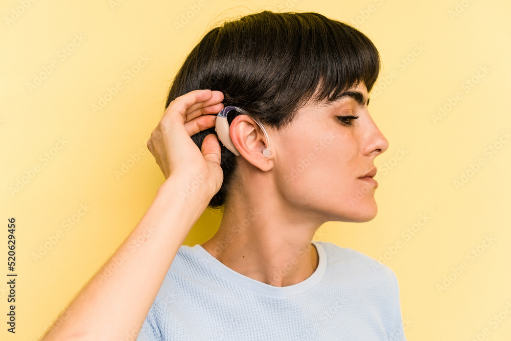 Young caucasian woman wearing a hearing aid isolated on yellow background Young caucasian woman wearing a hearing aid isolated on yellow background