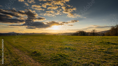 Romantic sunset on a field in northern Bohemia. Sky is calm and with few clouds and sun above the horizon.