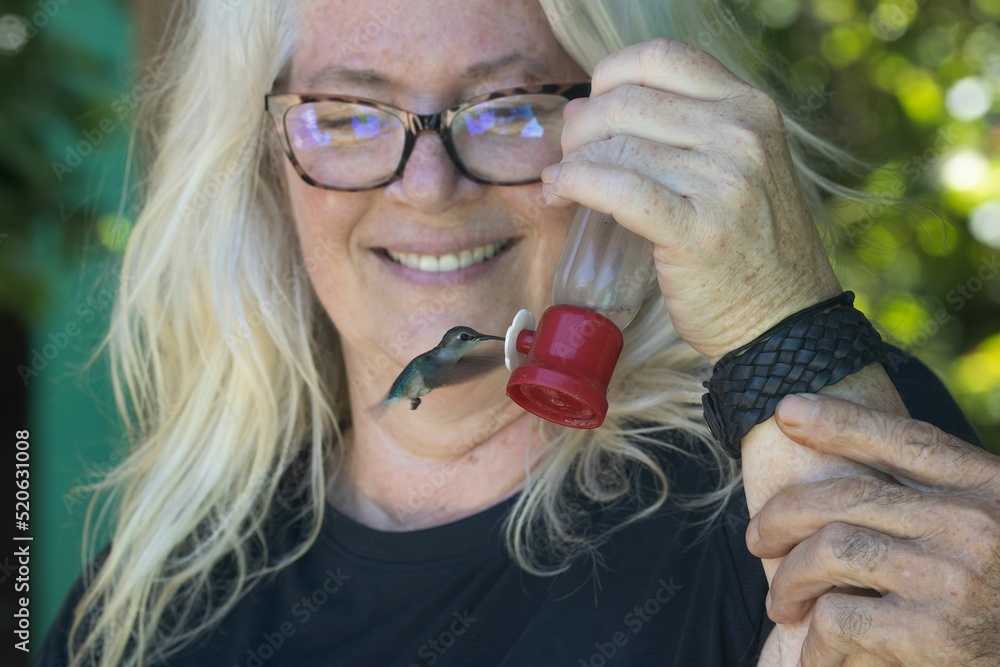 Fototapeta premium Smiling woman holding a feeder for a hummingbird