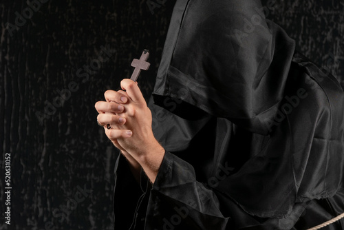A monk praying with a rosary and crucifix in his hand.