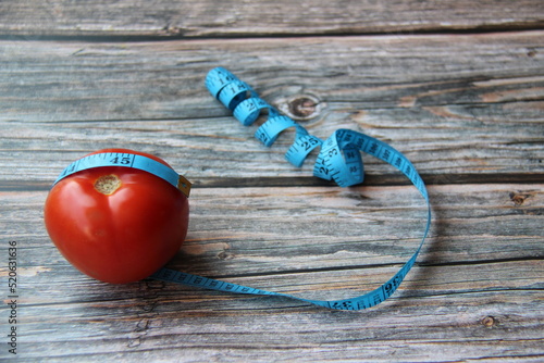 Measuring tape wrapped around a red tomato, on a wooden table, top view with text space. photo