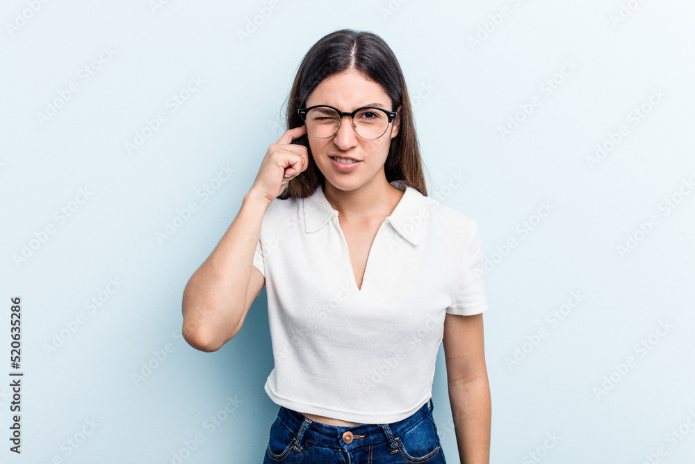 Young caucasian woman isolated on blue background covering ears with fingers, stressed and desperate by a loudly ambient. Young caucasian woman isolated on blue background covering ears with fingers, stressed and desperate by a loudly ambient.