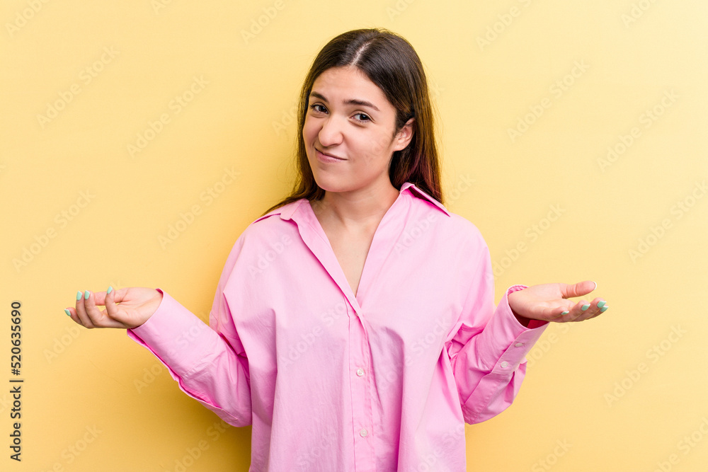 Young caucasian woman isolated on yellow background doubting and shrugging shoulders in questioning gesture. Young caucasian woman isolated on yellow background doubting and shrugging shoulders in questioning gesture.