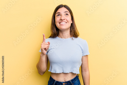 Young caucasian woman isolated on yellow background indicates with both fore fingers up showing a blank space.