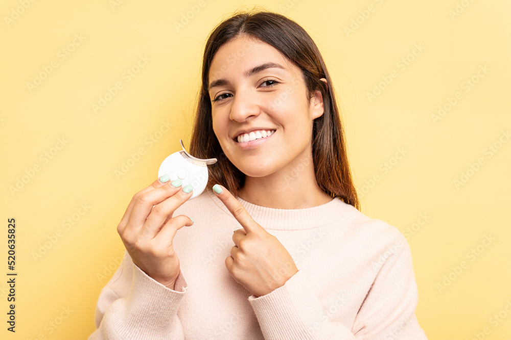 Young caucasian woman holding teeth whitener isolated on yellow background Young caucasian woman holding teeth whitener isolated on yellow background