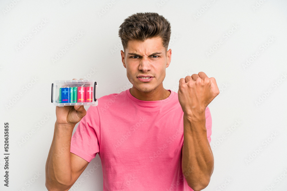 Young caucasian man holding a batteries box isolated on white background showing fist to camera, aggressive facial expression. Young caucasian man holding a batteries box isolated on white background showing fist to camera, aggressive facial expression.