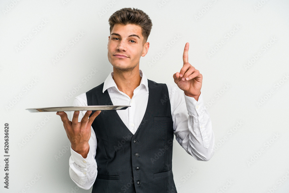 Young caucasian waitress man holding a tray isolated on white background showing number one with finger. Young caucasian waitress man holding a tray isolated on white background showing number one with finger.