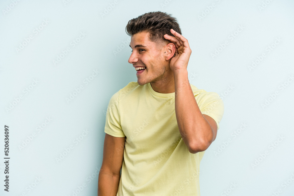 Young caucasian man isolated on blue background trying to listening a gossip. Young caucasian man isolated on blue background trying to listening a gossip.