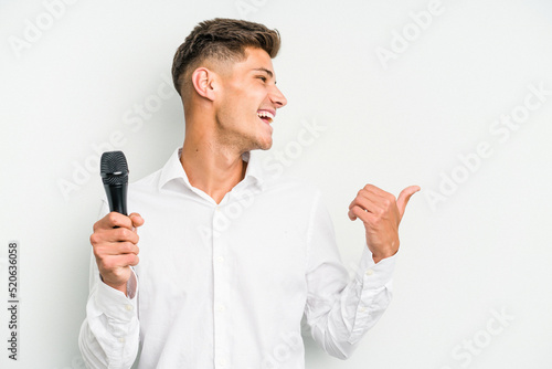 Young singer caucasian man isolated on white background points with thumb finger away, laughing and carefree.
